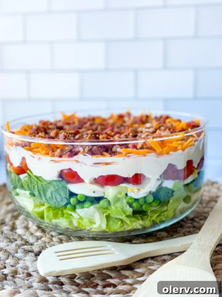 Classic Seven-Layer Salad 2 A vibrant, neatly layered 7 Layer Salad presented in a clear glass trifle dish, showcasing its colorful ingredients.