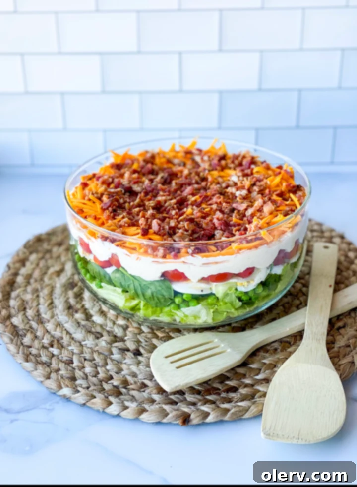Classic Seven-Layer Salad 5 The 7 layer salad in a glass bowl, showcasing the distinct layers, with a serving spoon ready to scoop.