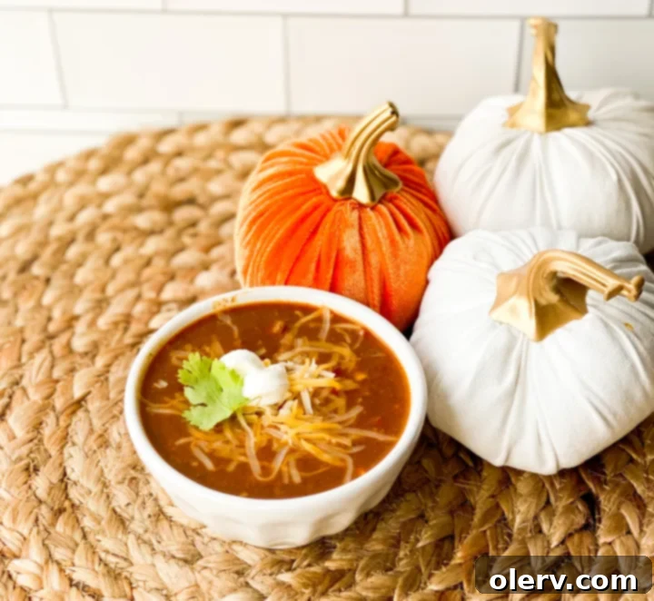 Hearty Pumpkin Chili Recipe 6 A serving of pumpkin chili in a bowl, topped with shredded cheese and a dollop of sour cream.
