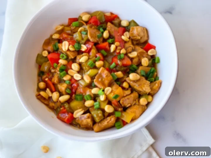 Speedy Instant Pot Kung Pao Chicken 5 A beautifully plated serving of Instant Pot Kung Pao Chicken in a white bowl, garnished with toasted peanuts and fresh green onions, with a side of perfectly steamed white rice.