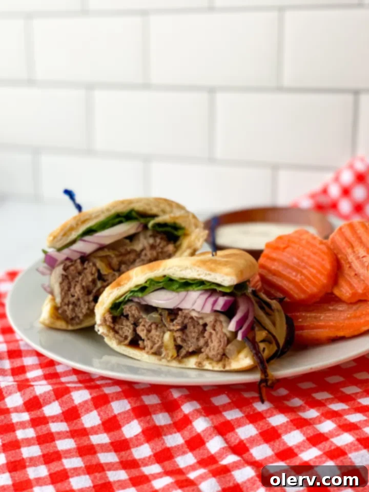 Perfect Air Fryer Burgers 8 A close-up of a fully assembled air fryer hamburger on a pita, topped with Swiss cheese, lettuce, and onions.
