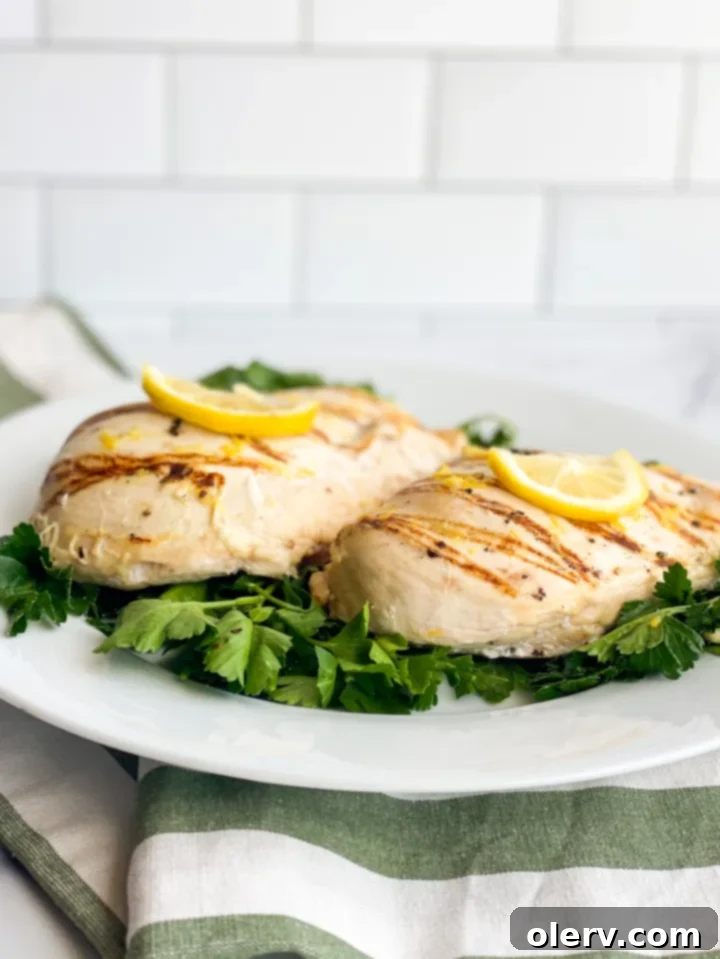 All fresh ingredients for Greek Lemon Chicken, including lemons, garlic, parsley, and chicken breasts, arranged on a wooden board.