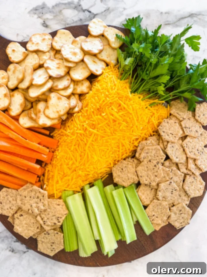 The finished Easter Carrot Cheese Ball surrounded by a variety of dippers including crackers, pretzels, and fresh vegetables on a white serving platter.