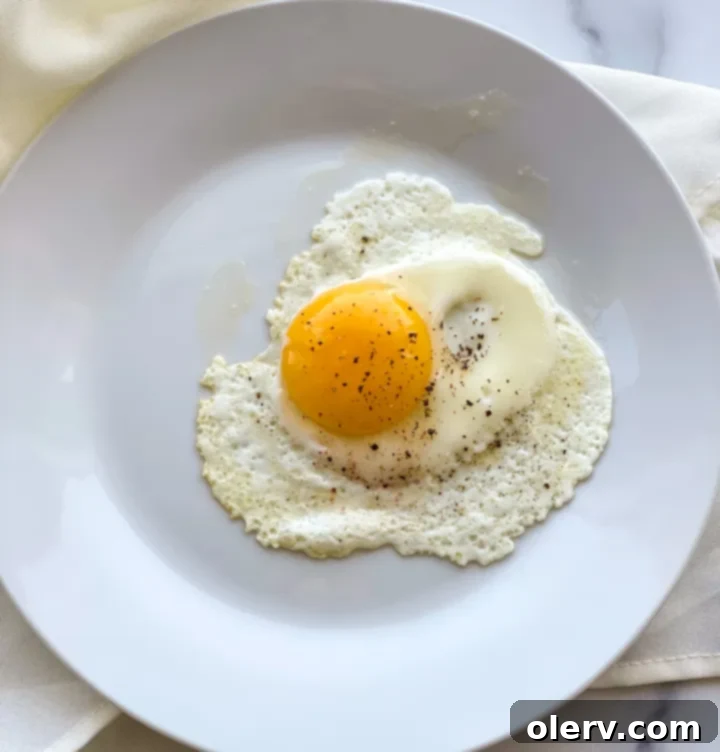 Mastering the Egg 5 A perfectly cooked sunny side up egg with a vibrant, runny yolk, served with a piece of toast on a white plate