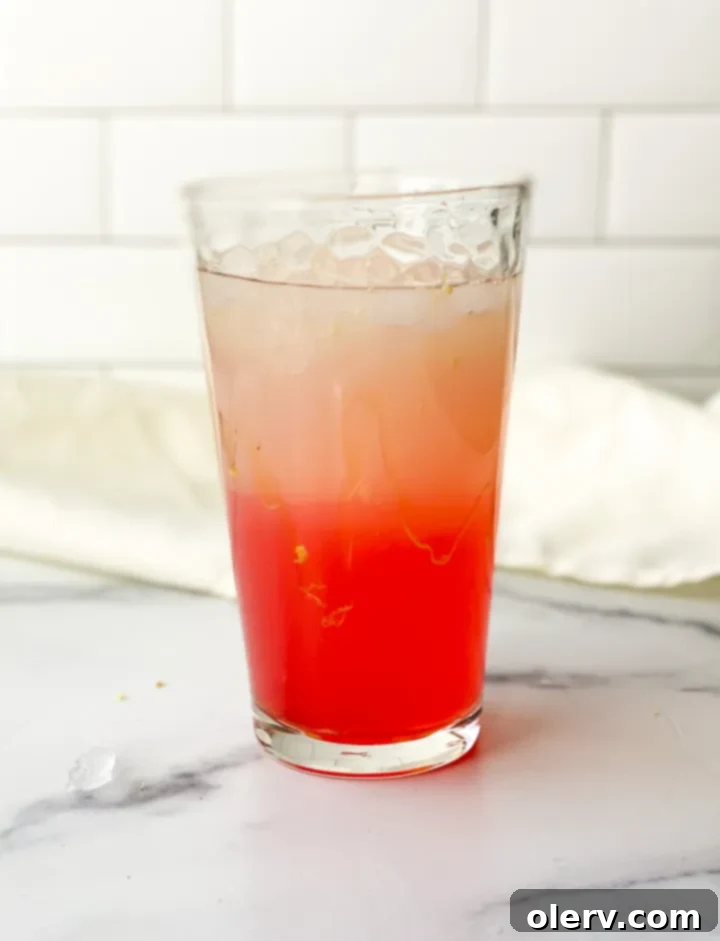 A tall glass of pink hibiscus lemonade garnished with lemon slices and ginger, inviting readers to pin the recipe.