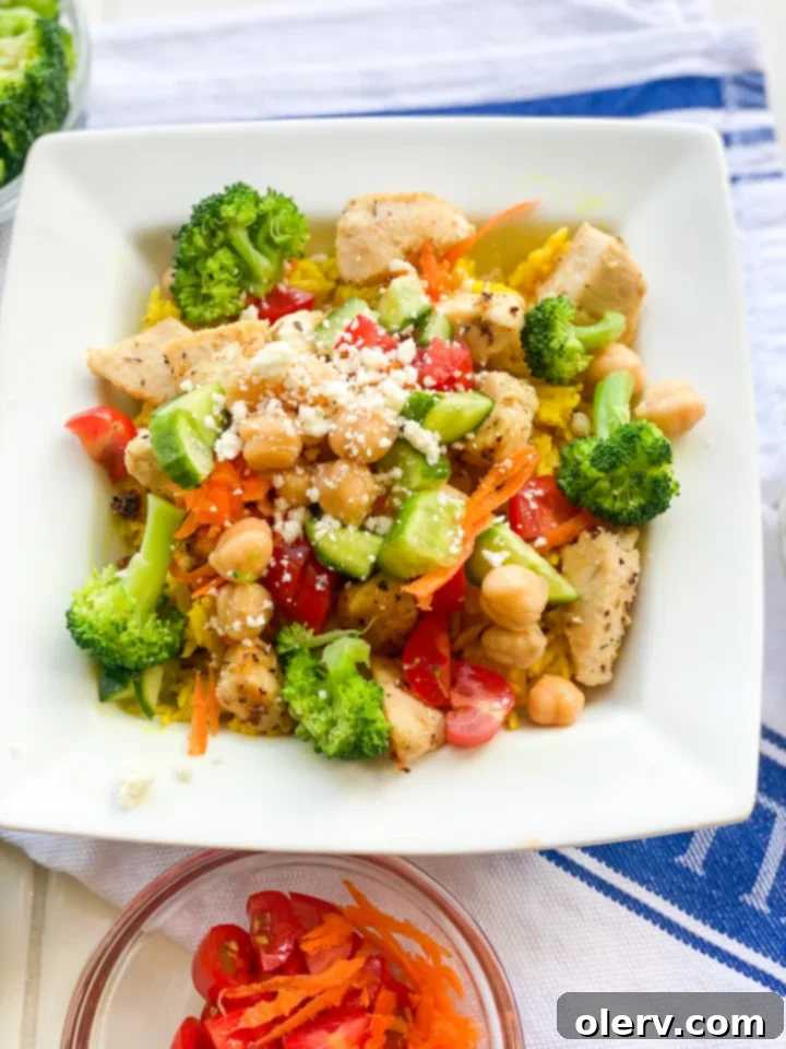 Greek Chicken Bowls 6 A perfectly assembled Greek Chicken Bowl with various fresh toppings and a side of sauce.