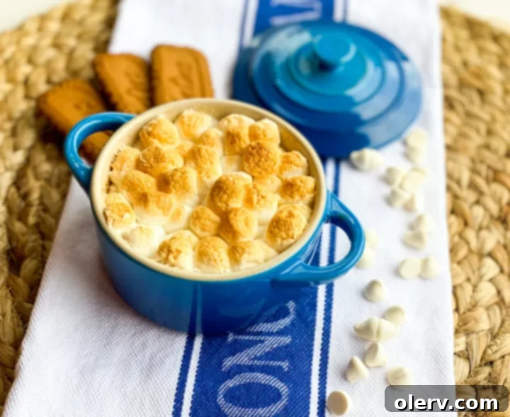 Caramelized Biscoff Smore Cups 5 A mini blue Le Creuset dutch oven filled with Biscoff S'more Cup ingredients and a spoon, against a light background.