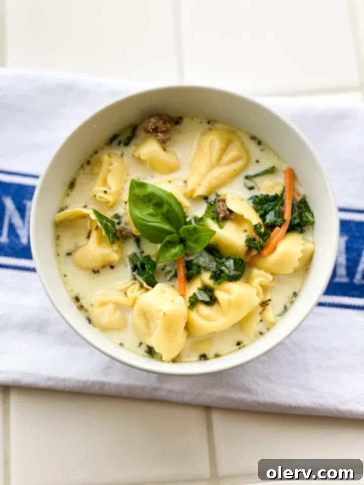 Creamy tortellini sausage soup in a bowl, garnished with fresh herbs.