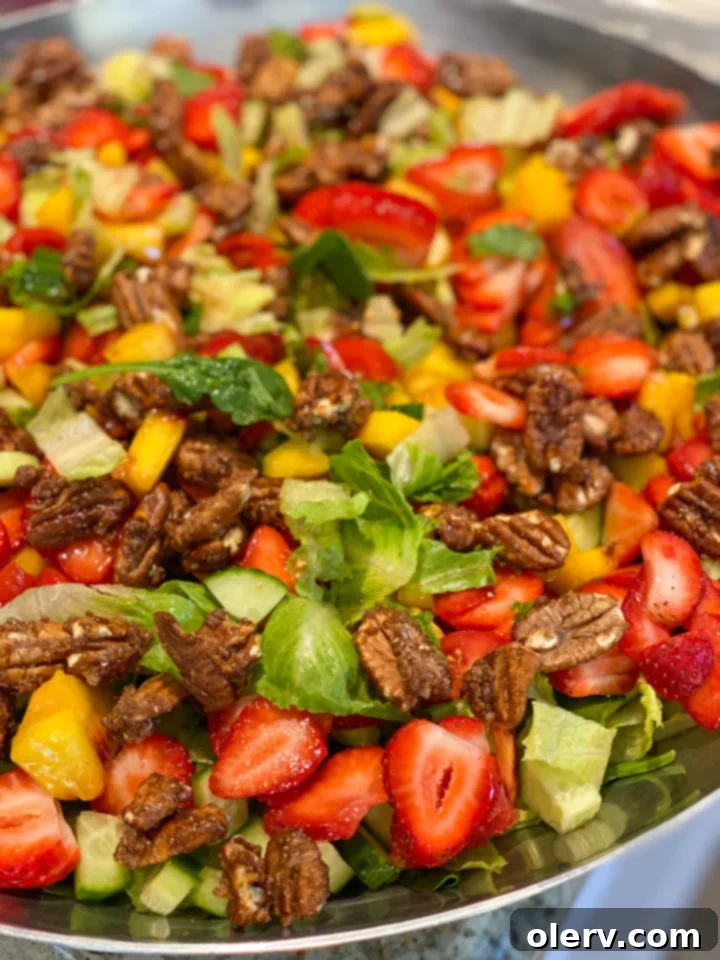 Vibrant Spinach Strawberry Salad 5 A hand gently tossing the colorful Spinach Strawberry Salad in a large glass bowl, showcasing the fresh greens, fruits, vegetables, and candied pecans mixing together.