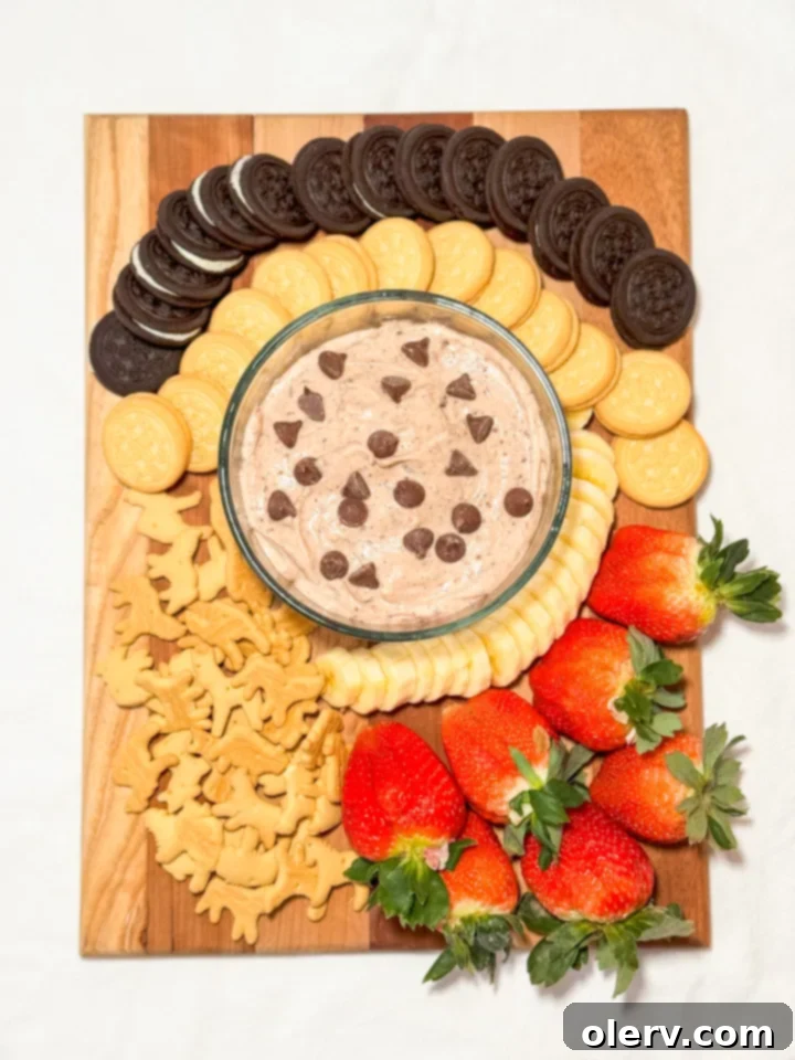 Irresistible Chocolate Chip Dip 3 Overhead shot of a beautifully arranged sweet charcuterie board with a central bowl of creamy chocolate chip dip, surrounded by fresh fruits, various cookies, and pretzels.