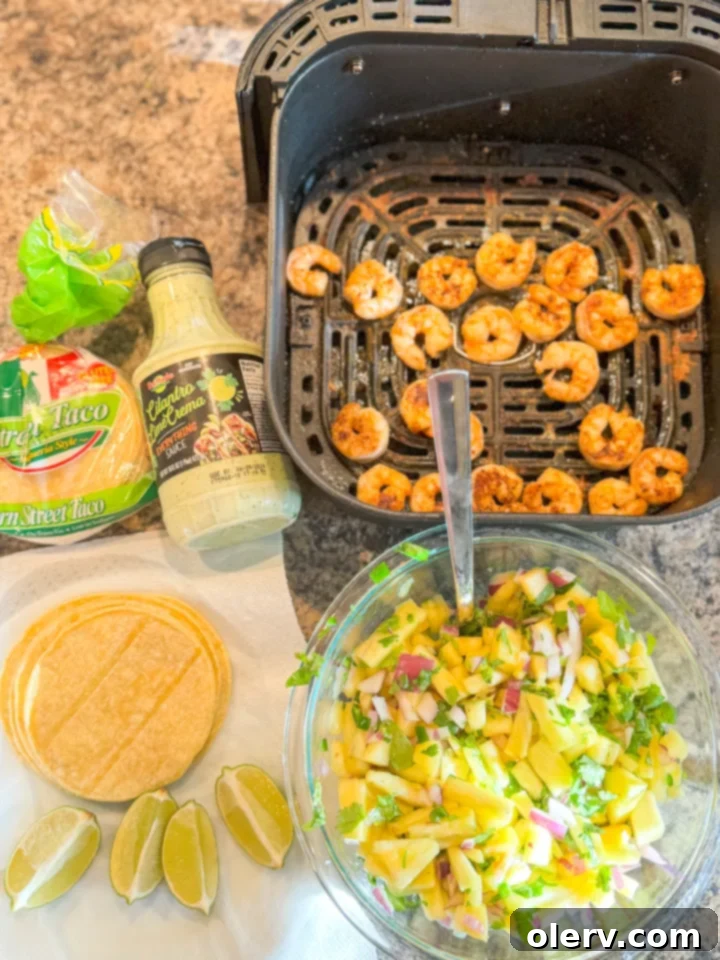 Crispy Air Fryer Shrimp Tacos 6 Assembled air fryer shrimp tacos with avocado slices, lime wedges, and a bowl of pineapple salsa