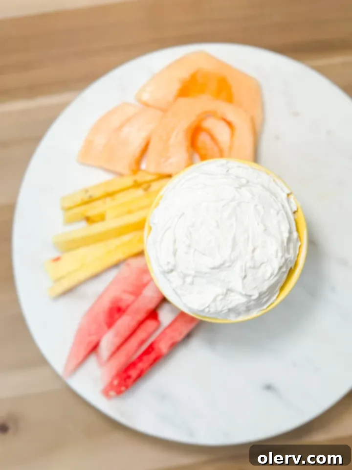 Quick Creamy Fruit Dip 5 A hand dipping a fresh strawberry into the creamy, white fruit dip, demonstrating its smooth and inviting texture.