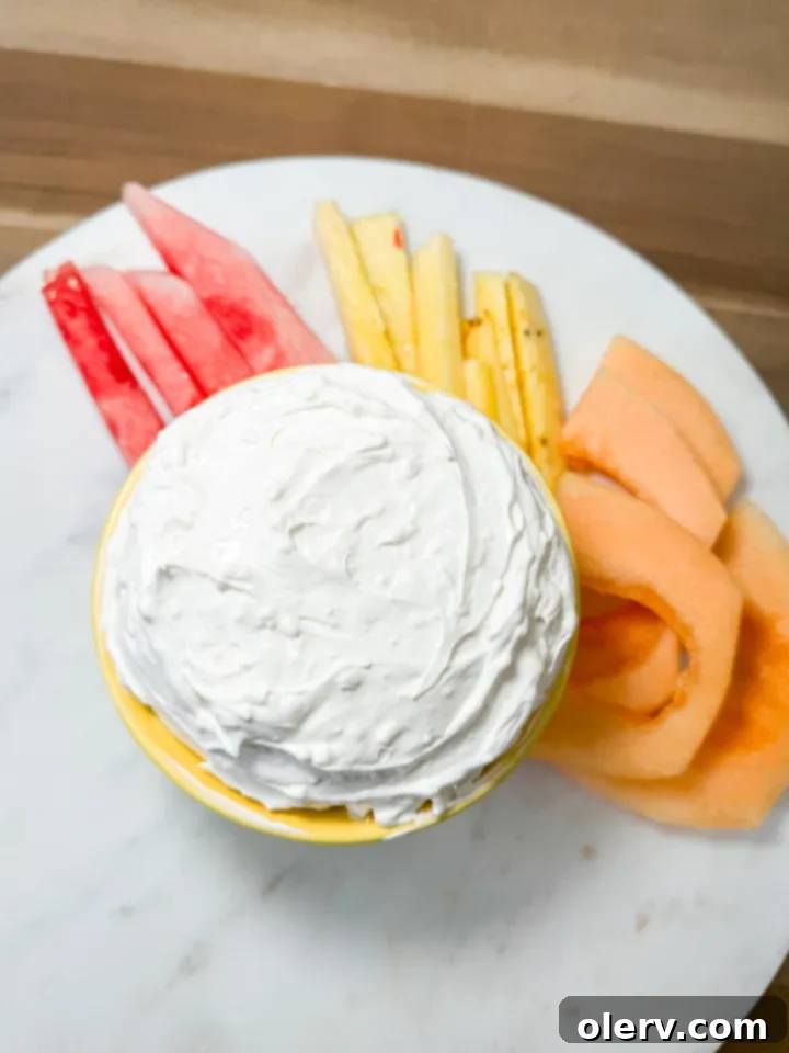 Quick Creamy Fruit Dip 6 A generous scoop of the easy fruit dip served in a rustic bowl, surrounded by a vibrant selection of fruits and cookies, ready for a party.