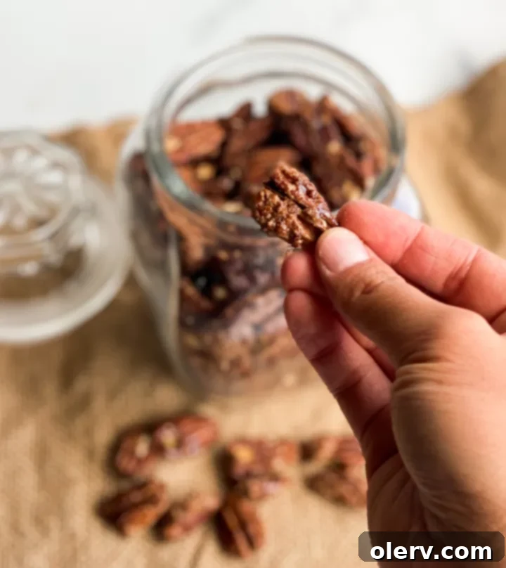 Irresistible Candied Pecans 4 A hand reaching into a bowl of candied pecans, showcasing their texture.