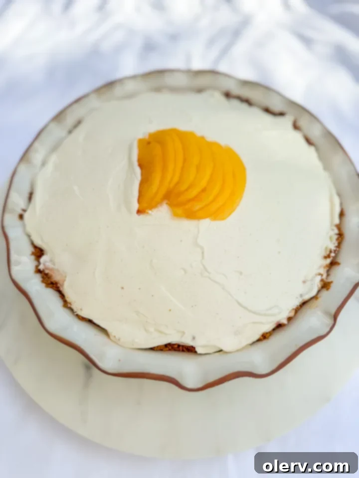 Creamy No-Bake Peach Delight 3 Close-up of a whole no-bake peach cream pie with fresh peach slices and whipped cream topping.