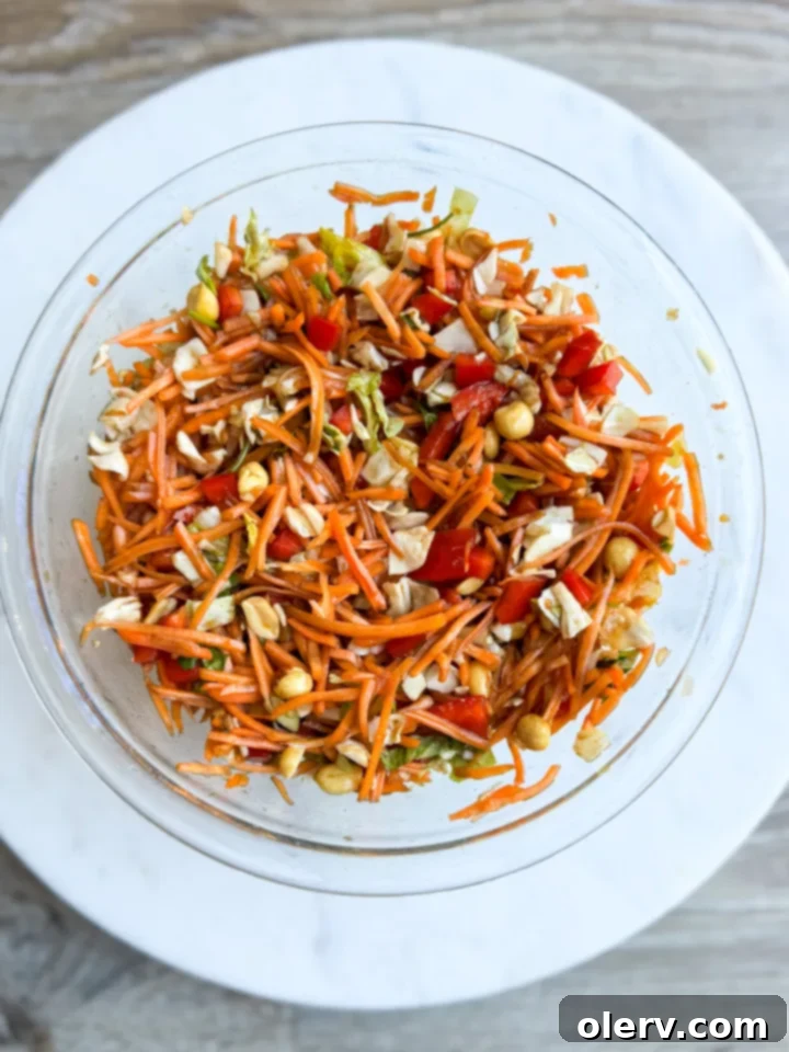 A vibrant bowl of Thai Crunch Carrot Salad, brimming with shredded carrots, cabbage, bell peppers, cilantro, and peanuts, topped with a sweet soy dressing.