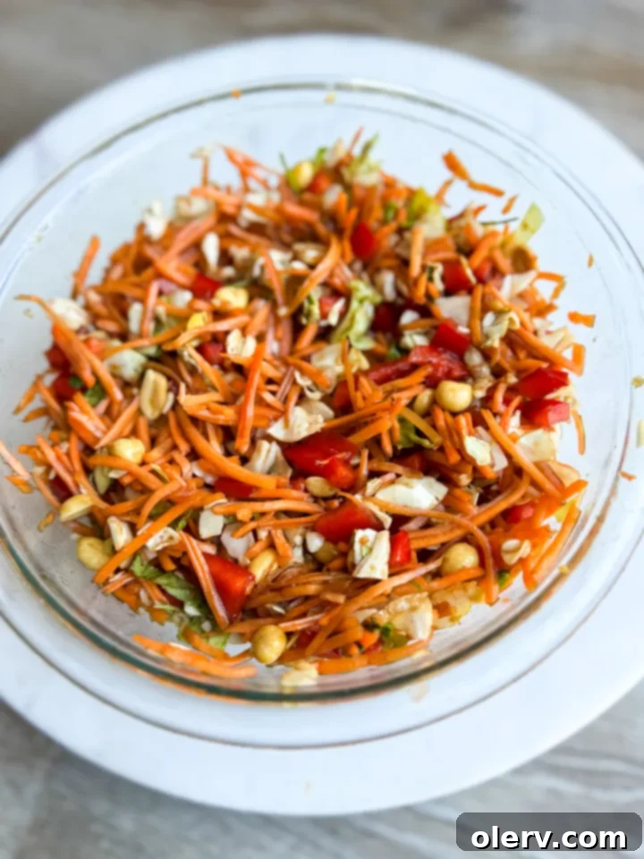 Close-up of fresh, colorful vegetables like shredded carrots, cabbage, and diced red bell pepper, ready for the Thai Crunch Carrot Salad.