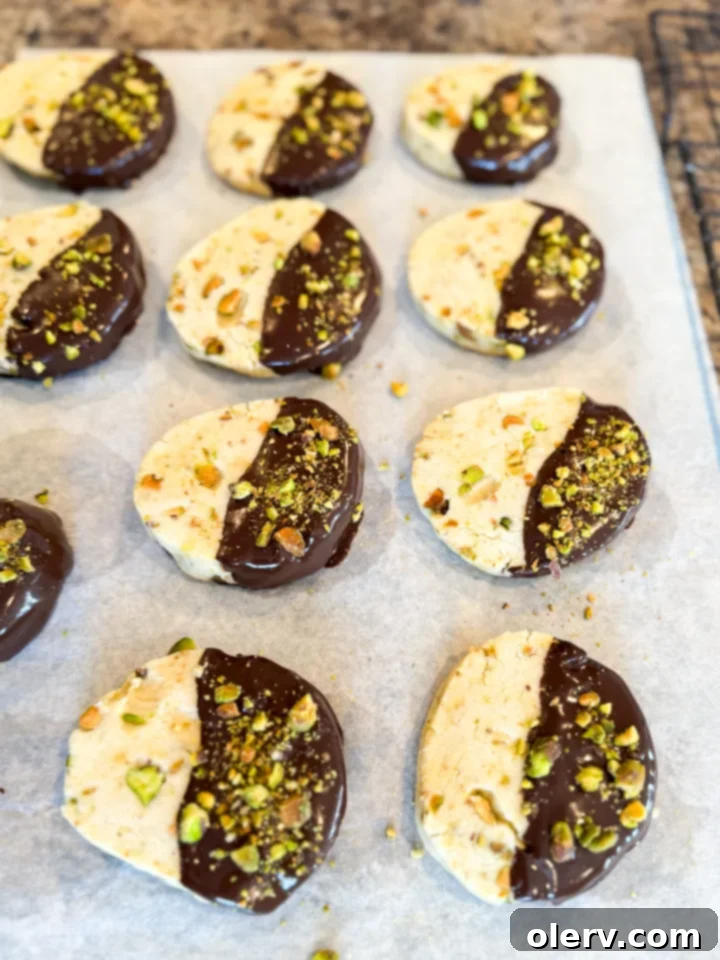 Buttery Pistachio Shortbread Cookies 5 Pistachio shortbread cookies dipped in chocolate with pistachios sprinkled on top, arranged neatly.