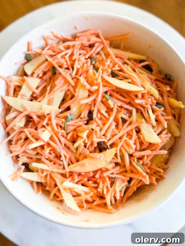 Vibrant Carrot Slaw 3 Close-up of fresh ingredients for Carrot Slaw Salad: shredded carrots, apple sticks, raisins, and pumpkin seeds.