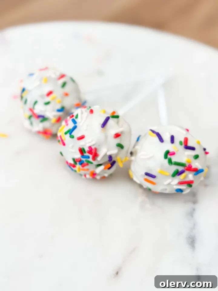 Close-up of a beautifully coated funfetti cake pop, glistening with white chocolate and colorful sprinkles, ready to be enjoyed.