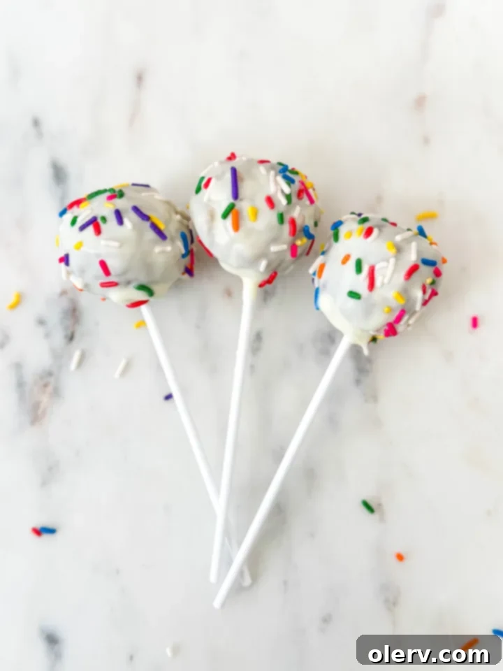 Several cake pops in various stages of preparation, with some ready for dipping and others already coated with chocolate and sprinkles.