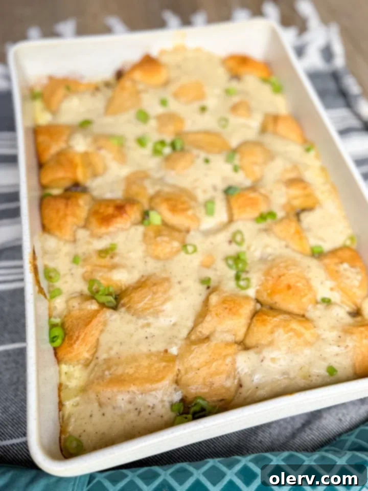 Hearty Biscuits and Gravy Bake 4 A baking dish filled with layers of Biscuits and Gravy Casserole ingredients before baking, with biscuit pieces on top.