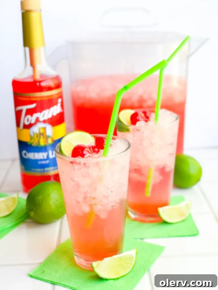 Crimson Zest Sparkle 6 Torani Cherry Lime syrup bottle next to a glass of Sparkling Cherry Limeade with lime and cherries