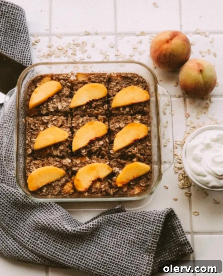 Sweet Peach Baked Oatmeal 5 A slice of peach baked oatmeal on a white plate, garnished with fresh peach slices and a dollop of Greek yogurt