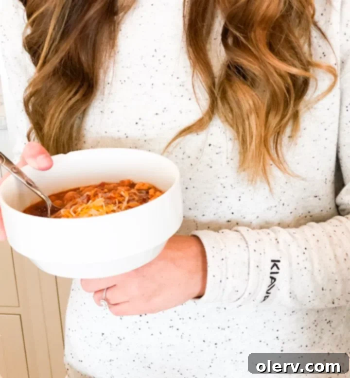 Hearty, Healthy Turkey Chili 3 The blogger smiling, holding a bowl of chili, dressed in stylish workout wear.