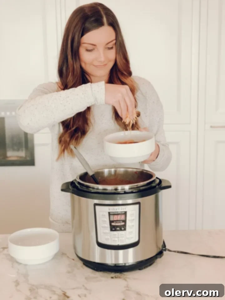 Hearty, Healthy Turkey Chili 9 A person pouring chicken broth into an Instant Pot with sautéed onions and ground turkey.