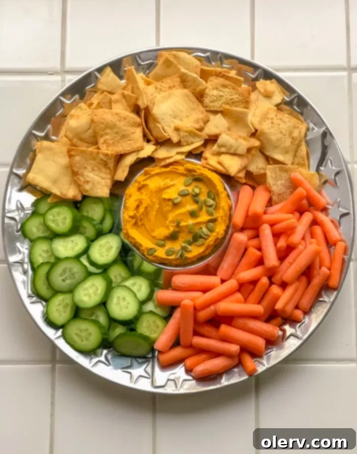 Savory Pumpkin Hummus garnished with olive oil and pumpkin seeds, served with fresh cucumber and carrot sticks