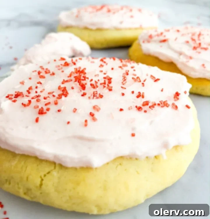 Tender Sour Cream Sugar Cookies 5 A hand holding a round, frosted sour cream sugar cookie with pink frosting and colorful sprinkles.