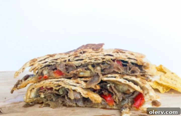 Philly Cheesesteak Crunchwrap 2 Crispy golden brown Philly Cheesesteak Crunch Wrap cut in half, revealing gooey cheese, tender steak, and sautéed vegetable filling