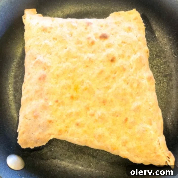 Philly Cheesesteak Crunchwrap 8 A Philly Cheesesteak Crunch Wrap toasting in a hot frying pan, showing a golden brown crust forming on the seam side