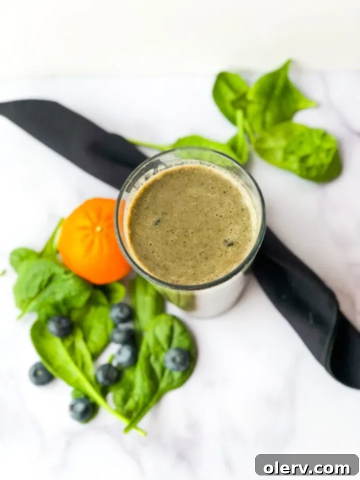 Nature's Immunity Elixir 4 A green smoothie in a glass with a straw, garnished with fresh fruit, on a kitchen counter.