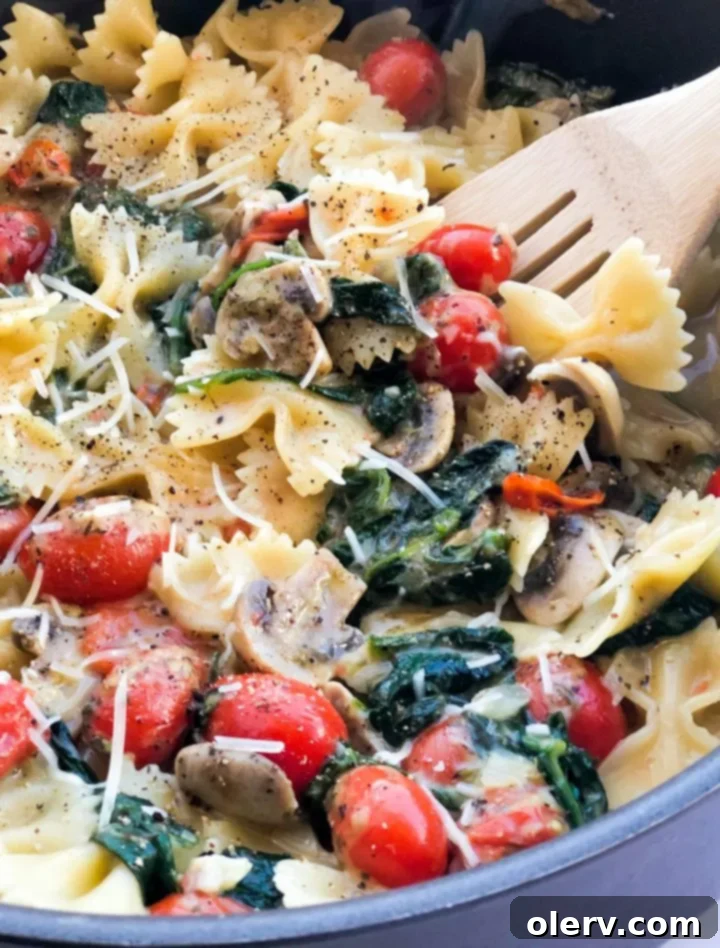 Delicious Meatless Mushroom Spinach Pasta 3 Fresh ingredients for mushroom spinach pasta, including mushrooms, spinach, cherry tomatoes, and farfalle, arranged on a rustic wooden table