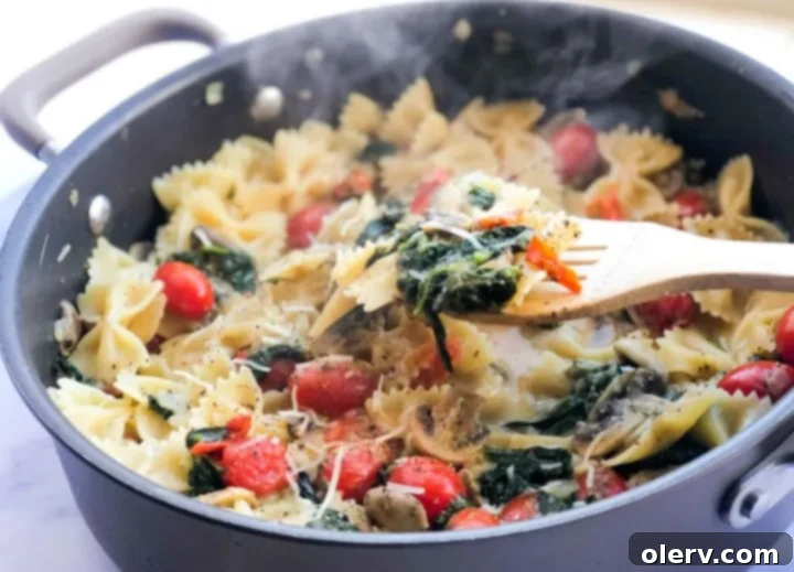 Delicious Meatless Mushroom Spinach Pasta 4 Mushroom spinach pasta being tossed in a large skillet with a wooden spoon, showcasing the vibrant colors of the vegetables
