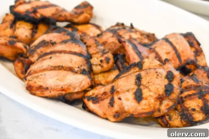 Grilled chicken on a wooden cutting board with fresh herbs.