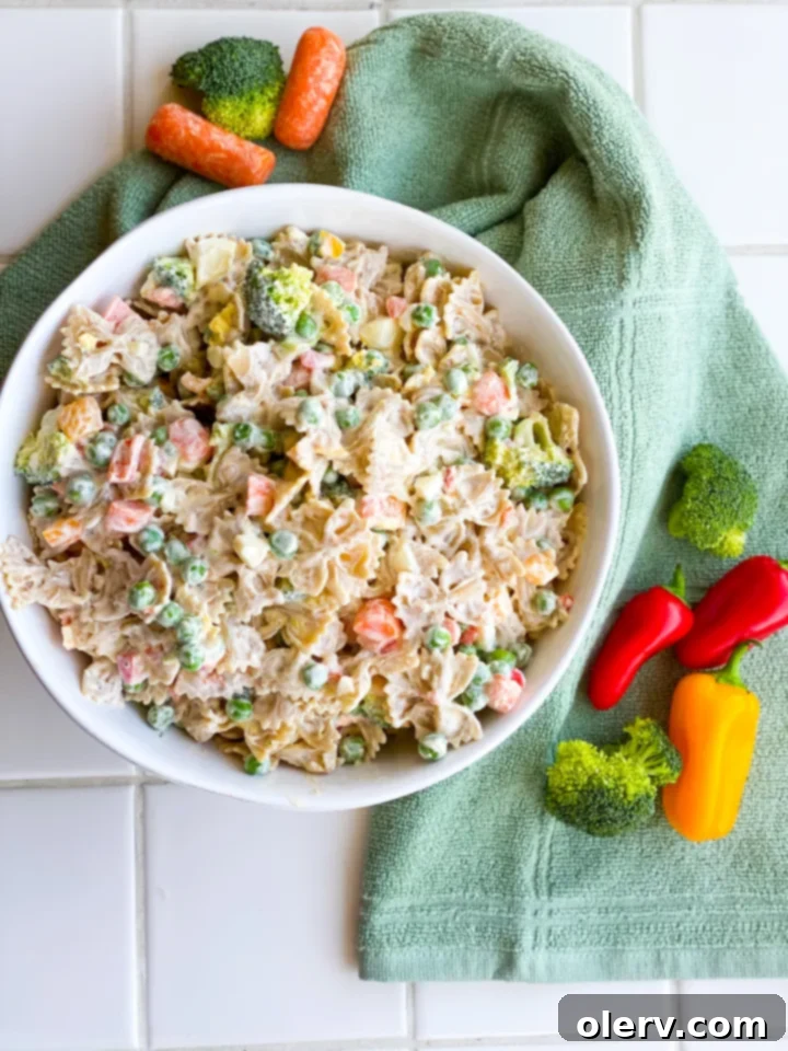 Velvety Farfalle Pasta Salad 4 A bowl of creamy pasta salad with bow tie noodles and vegetables, with a hand mixing the dressing.