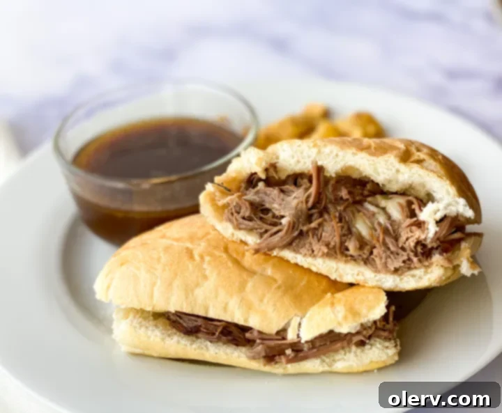 Ultimate Slow Cooker French Dip Sandwiches 2 Perfectly assembled Slow Cooker French Dip sandwich with melted Swiss cheese on a toasted hoagie bun, ready for dipping into au jus.