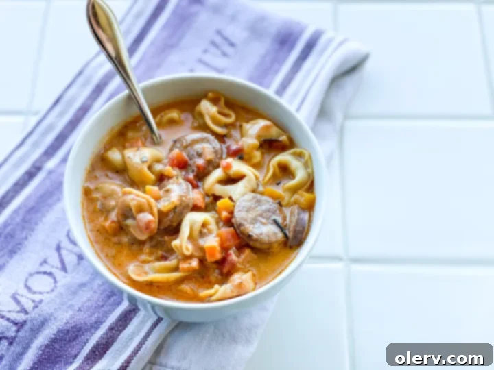 Hearty Sausage and Tortellini Soup 6 A close-up of creamy sausage and tortellini soup in a bowl with a spoon.