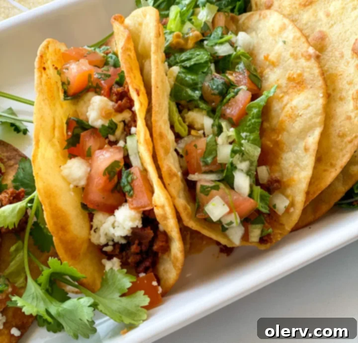 Close-up of a corn tortilla being held open with tongs while frying in hot oil, forming a perfect taco shell.