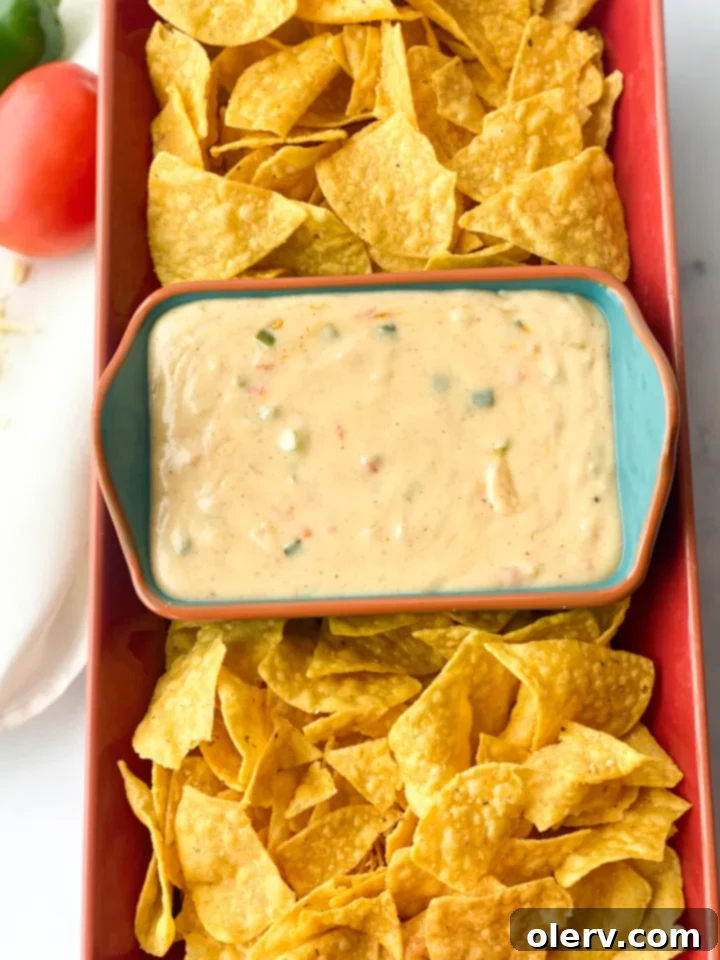 Chipotle Queso Blanco Copycat 7 A hand dipping a tortilla chip into a bowl of creamy Queso Blanco.