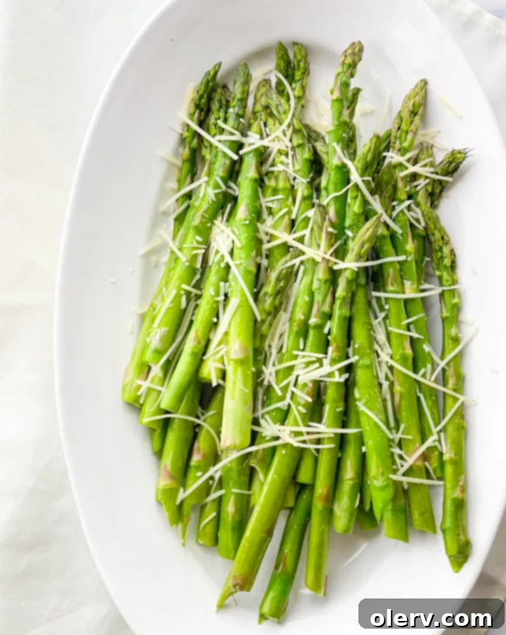 A vibrant close-up of air-fried asparagus spears on a plate, garnished with fresh herbs and a lemon wedge.