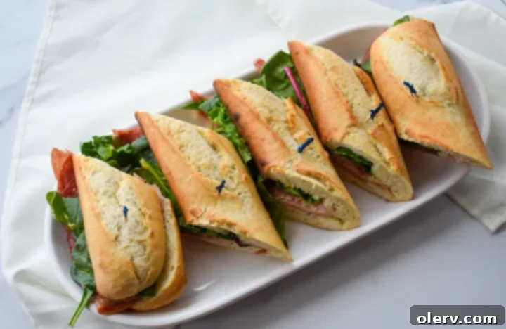 Artisan Baguette 5 All the fresh ingredients for the baguette sandwich laid out, including a French baguette, deli ham, salami, brie cheese, garlic butter, Dijon mustard, and vibrant greens.