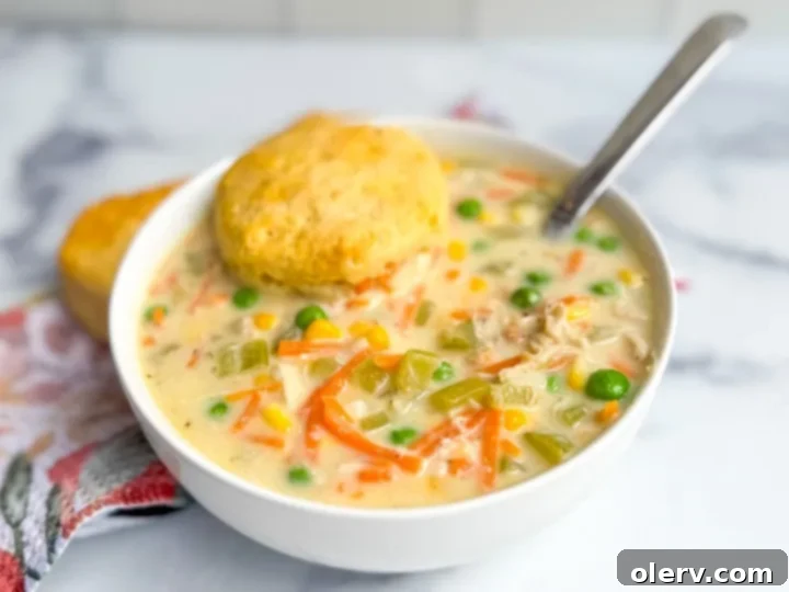 Two bowls of creamy chicken pot pie soup, garnished with fresh herbs and fluffy biscuits